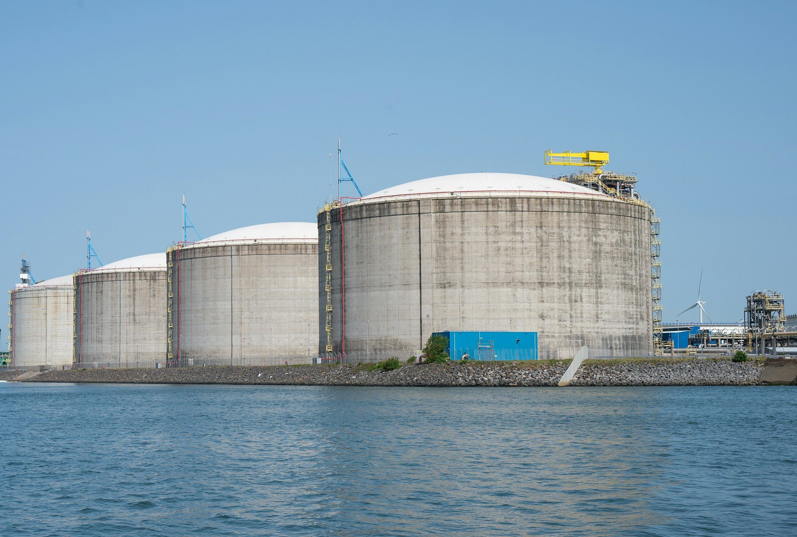 LNG storage tanks on a waterfront terminal under a clear sky